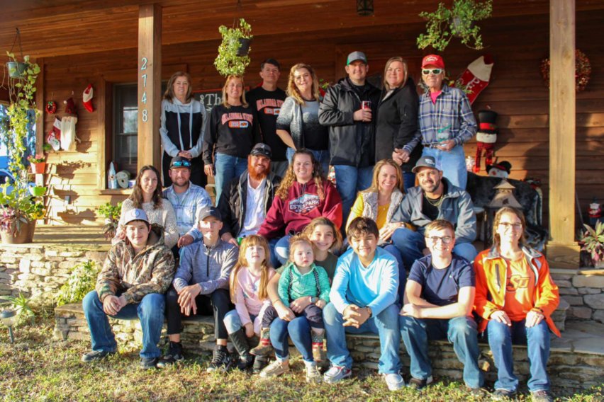 A group of people sitting on the ground in front of a house.