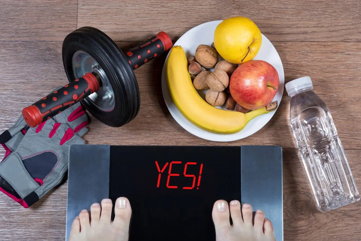 A person standing on their scale with an apple, banana and nuts.